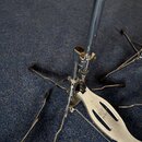 Detailní pohled na spodní část kovového stojanu s nožkami a pedálem v stříbrné barvě. Povrch kovových částí vykazuje známky opotřebení a drobné škráb…