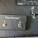 Černý dvoukanálový nožní spínač s nápisem Blackstar. Na panelu jsou dvě stisknutelná tlačítka označená písmeny A a B. Zařízení je umístěno na černém…