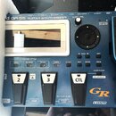 Modrý kytarový syntetizátor s nápisem GR-55 GUITAR SYNTHESIZER a logy GR a COSM. Zařízení má digitální displej, několik ovládacích tlačítek v sekcích…