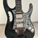 Černá elektrická kytara s výrazně vyřezaným tělem a bílo-šedým mramorovaným pickguardem. Na hmatníku je v horní části nápis STEVE VAI. Nástroj má tři…