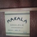 Detail štítku uvnitř těla ukulele. Na béžovém podkladu je černý nápis MAKALA UKULELE a webová adresa www.kalaukulele.com. U označní MODEL NO: je ručn…