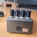 Šedý efekt pedál s kovovým povrchem a čtyřmi černými oválnými knoflíky. Na horní části jsou vidět nápisy MODULATE, SETTINGS a CHECK u červené kontrol…