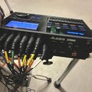 Černý elektronický modulAlessis STRIKE s modře podsvíceným displejem a ovládacími prvky. Na předním panelu jsou nápisy ALESIS STRIKE, MIDI OUT, MIDI…