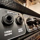 Detailní pohled na ovládací panel kytarového zesilovače. Jsou vidět dva vstupy s nápisy INPUTS, HIGH GAIN a LOW GAIN. Vedle nich se nachází sekce CLE…