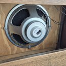 Kruhový reproduktor s kovovým šedým rámem a magnetem, umístěný v dřevěné bedně. Na bílém štítku magnetu je nápis SUPER 65f a pod ním menší text v rám…
