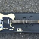 Elektrická kytara typu Telecaster v krémové barvě s černým pickguardem, položená v černém tvrdém kufru. Na hlavě hmatníku je žlutý lak a nápisy Fende…