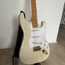 Krémově bílá elektrická kytara typu Stratocaster s bílým pickguardem a javorovým hmatníkem. Nástroj má tři snímače, zlatý kobylník a zlaté ovládací k…