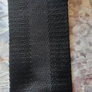 Detailní záběr na černý textilní popruh z tkaniny s výraznou strukturovanou vazbou. Materiál vykazuje drobné známky opotřebení v podobě drobných vlák…