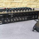 Černý mixážní pult značky TASCAM s dřevěnými bočními panely. Na předním panelu je nápis Model 16 a řada ovládacích prvků, včetně knoflíků v červené,…