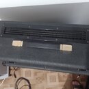 Černý kytarový kombozesilovač nebo box s povrchem z texturované vinylové krytiny. Na horní straně je umístěna černá ventilační mřížka a madlo s kovov…