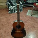 Akustická kytara s tělem v barevné variantě sunburst (přechod od žluté přes hnědou k černé). Nástroj má hnědý hmatník a tmavé ladící mechanismy na hl…