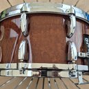 Fotografie znázorňuje snare drum s hnědým lakovaným dřevěným korpusem a chromovaným kováním. Na černém popasku je viditelný nápis "SOUND". Nástroj vy…