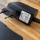 Černý síťový adaptér s evropskou vidlicí. Na štítku je uveden nápis BOSS SWITCHING ADAPTER, MODEL PSA-100S, INPUT: 100-240V~ 50-60Hz 200mA, OUTPUT: 9…