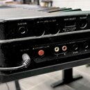 Zadní panel černého elektronického klávesového nástroje s několika konektory. V horní části jsou nápisy SUSTAIN, IN, MIDI, OUT, HOST SELECT a TO HOST…