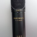 Černý kondenzátorový mikrofon s kovovou síťkou. Na těle je zlatý nápis KURZWEIL a pod ním bílý text It's the sound. Ve spodní části jsou bílá loga CE…
