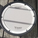 Fotografie znázorňuje elektronický buben s bílým mesh povrchem a černým obručem. Na membráně jsou nápisy „Roland“, „MESH HEAD“ a „Reg. U.S. Pat. & Tm…