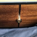 Detailní záběr na hranu dřevěného těla nástroje v hnědé barvě s viditnou strukturou dřeva. V boku je umístěn kovový zlatý konektor pro kabel. Nástroj…