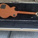 Elektrická kytara s hnědým lakem a tvarem Les Paul v otevřeném tvrdém kufru s černým vnitřkem. Na hlavě hmatníku je vidět nápis Gibson a sériové čísl…