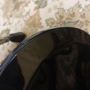 Detailní záběr na černý, lesklý povrch hudebního nástroje s zaobleným okrajem. Na povrchu jsou vidět drobné škrábance a prachové částice. Žádné značk…