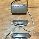 Tři elektrické snímače kytary s kovovými kryty v stříbrné barvě, umístěné na dřevěném povrchu. Horní snímač je typu humbucker s šesti viditelnými pol…