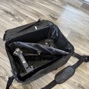 Otevřený černý transportní vak z textilního materiálu, ve kterém je umístěn bubenový pedál. Na pedálu je viditelný nápis MAPEX. Vak má připevněný čer…
