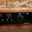 Červený audio rozhraní Scarlett Solo s černým předním panelem. Na panelu jsou dva menší a jeden velký ovládací knoflík, vstupní konektor jack, výstup…