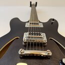 Černá polodupatá elektrická kytara s dvěma snímači typu humbucker a chromovaným hardwarem. Nástroj má dvě vyřezané otvory (f-holes) a tmavý povrch s…