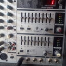 Detailní pohled na ovládací panel mixážního pultu BEHRINGER EUROPOWER PMH2000. Jsou vidět posuvníky ekvalizéru, ovládací prvky kanálů 9 a 10, digitál…