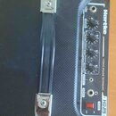 Černý basový kombozesilovač s nápisem Hartke a označením modelu HD25. Na ovládacím panelu jsou knofíky Volume, Bass, Mid a Treble, vstup AUX INPUT, v…