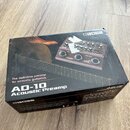 Kartonová krabice s produktem Boss AD-10 Acoustic Preamp. Na povrchu je zobrazen přístroj v hnědé barvě s ovládacími prvky a nápisy BOSS, AD-10, TUNE…