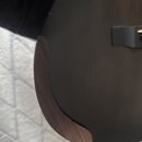 Detailní pohled na část těla kytary v matně černé barvě. Na hraně je vidět dřevěný lem s viditelnou strukturou zrna. Povrch nástroje vykazuje drobné…