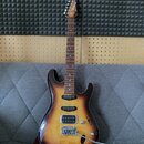 Elektrická kytara s trupem v barevně sunburst a hnedým hmatníkem. Na hlavě je vidět nápis Ibanez. Nástroj má dva humbuckery, jeden jednosmykový sníma…