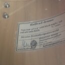 Detail vnitřní strany dřevěného korpusu bubnu s nalepeným bílým štítkem. Na štítku je text: „Hallvad drums“, „Tom tom 12" x 9" solid block maple / as…