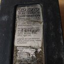 Fotografie zachycuje spodní stranu černého efekt pedálu. Uprostřed je nalepený papírový štítek s nápisy DOD ELECTRONICS CORPORATION, Sandy, Utah, U.S…