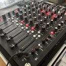 Černý DJ mixér s mnoha ovládacími prvky, včetně posuvníků a otočných knoflíků v černé a červené barvě. Na povrchu jsou bílé nápisy jako FILTER, SPLIT…