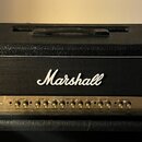 Černý kytarový kombozesilovač s texturovaným povrchem a bílým lemováním kolem přední mřížky. Na černé látce je bílý nápis Marshall a na zlatém ovláda…