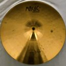 Zlatavý mosazný činel s centrálním otvorem. V horní části je černý nápis MAGIC a pod ním menší nápis BRASS. Povrch vykazuje drobné nečistoty a v doln…