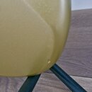 Detailní záběr na spodní část zlatého hudebního nástroje s matným povrchem. Nástroj je umístěn na černém kovovém stojanu. V dolní části povrchu nástr…