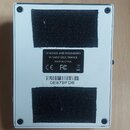 Zadní strana bílého čtvercového zařízení s dvěma černými plátěnými podložkami. Uprostřed je černý štítek s nápisy DESIGNED AND ENGINEERED IN SAINT GE…