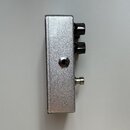 Stříbrný efektový pedál v kovovém obalu s matným povrchem. Na pravé straně jsou umístěny dva černé oválné ovládací knoflíky a jeden kovový spínač. Up…