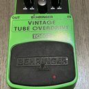 Zelený efekt pedál s černým ovládacím panelem a černou gumovou podložkou v dolní části. Na zařízení jsou nápisy BEHRINGER, VINTAGE TUBE OVERDRIVE a m…