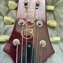 Hlava elektrické kytary v tmavě červené barvě s bílými ladičkami. Na povrchu je zlatý nápis Paul Reed Smith a modelové označení Mira X. Lak vykazuje…