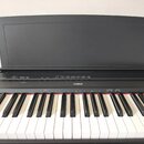 Černý digitální klavír se zvednutým víkem, na kterém je v horní části vyražen nápis YAMAHA. Na ovládacím panelu je uprostřed bílé logo a nápis YAMAHA…