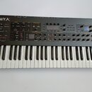 Černý syntetizátor s klaviaturou a ovládacím panelem s mnoha knoflíky, tlačítky a displeji. V levém horním rohu je bílý nápis SEQUENTIAL PROPHET X. P…