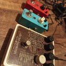 Tři efektové pedály umístěné na dřevěném povrchu. V popředí je bílý pedál s nápisy electro-harmonix, NEW YORK CITY, USA a organ machine, který obsahu…