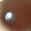 Fotografie zachycuje pohled do vnitřku dutého dřevěného nástroje s hnědým povrchem. V centru je vidět nepravidelný průnik v podobě otvoru s hrubým, n…