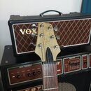 Fotografie zachycuje hmatník a hlavu elektrické kytary v přirozené dřevěné barvě. Na hlavě je viditelné logo v podobě podpisu a nápis VOX na předním…