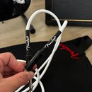 Bílý instrumentální kabel s černými konektory. Na obou černých krytech je bílý nápis Fender®. Kabel je v ruce, v pozadí je vidět černá taška s červen…