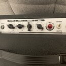 Detail ovládacího panelu kytarového komba s bílým pozadím a černým textem. Panel obsahuje čtyři otočné knoflíky s popisky VOLUME, TREBLE, MIDDLE a BA…