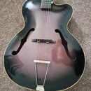 Elektrická polodupatá kytara s tmavým sunburst povrchem a dvěma f-otvory. Nástroj má hnědý dřevěný krk s hnedým hmatníkem a stříbrný mostek. Povrch t…